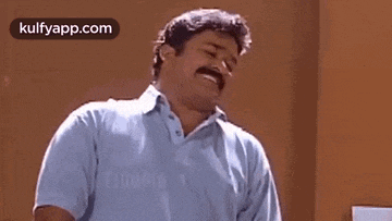 a man with a mustache and a blue shirt is standing in front of a wall .