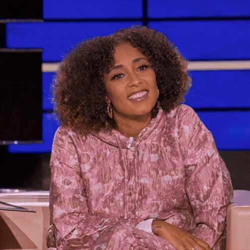 a woman with curly hair is smiling and wearing a pink floral dress