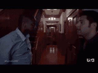 a man in a suit and tie is standing in a hallway talking to another man .