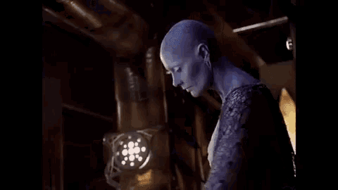 a woman with a blue face is standing in a dark room .