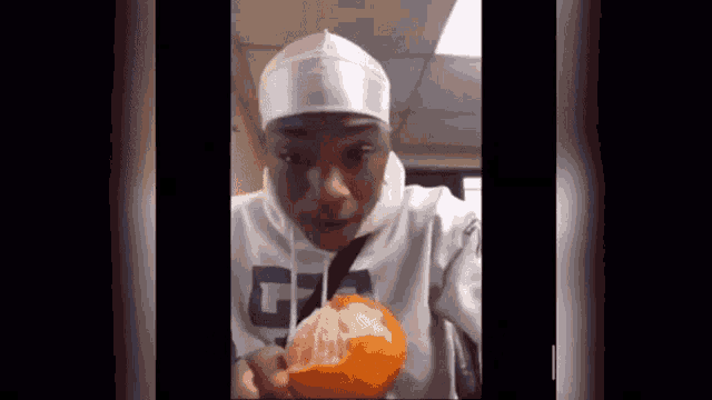 a man wearing a white headband is eating a half peeled orange .