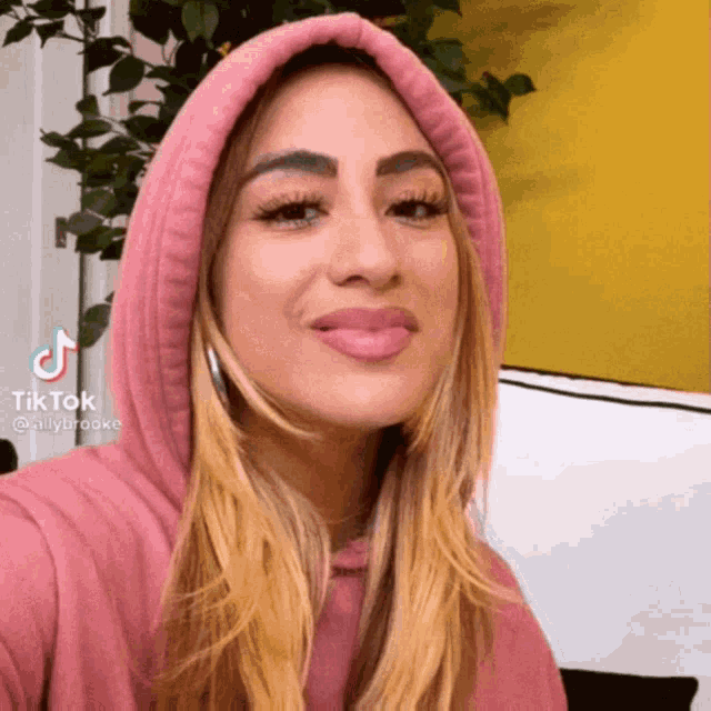 a woman wearing a pink hoodie has a tiktok watermark on her face