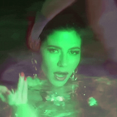 a woman is swimming in a bathtub with a green light behind her .