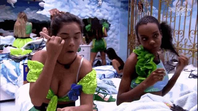 two women are applying makeup in a room that says big brother brasil on the wall
