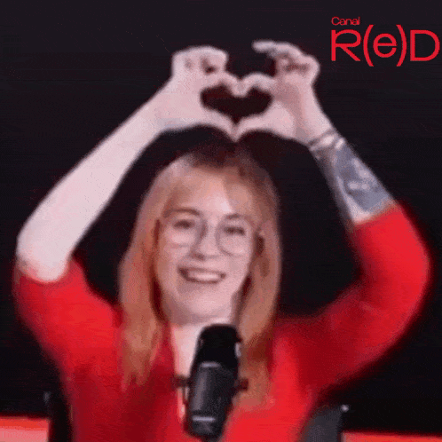 a woman in a red shirt and glasses is making a heart shape with her hands .