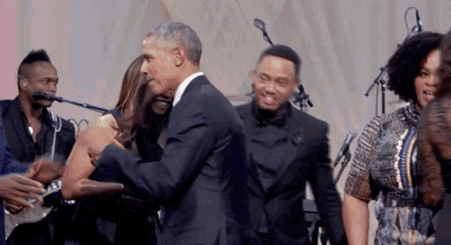 a man in a suit is hugging a woman in front of a group of people