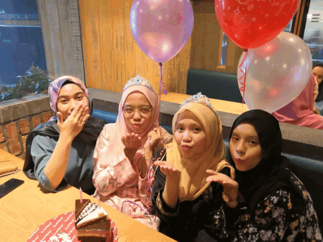 four women wearing tiaras pose for a picture in front of balloons that say i love you