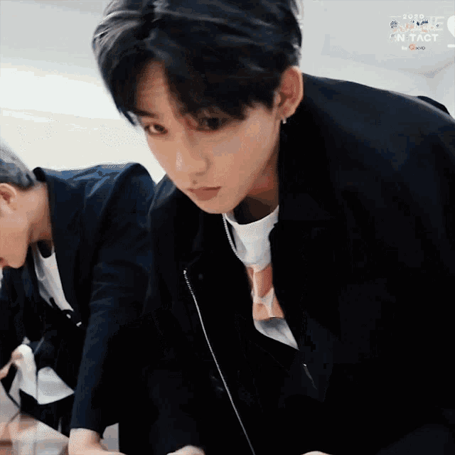 a man in a black jacket is looking down at something while another man looks on