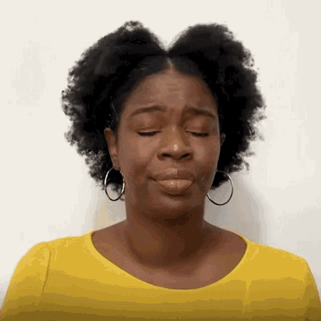 a woman wearing a yellow shirt and earrings is making a funny face .