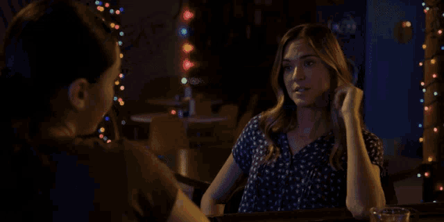 a woman sitting at a table talking to another woman in a dark room