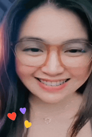 a woman wearing glasses and a necklace smiles with hearts around her