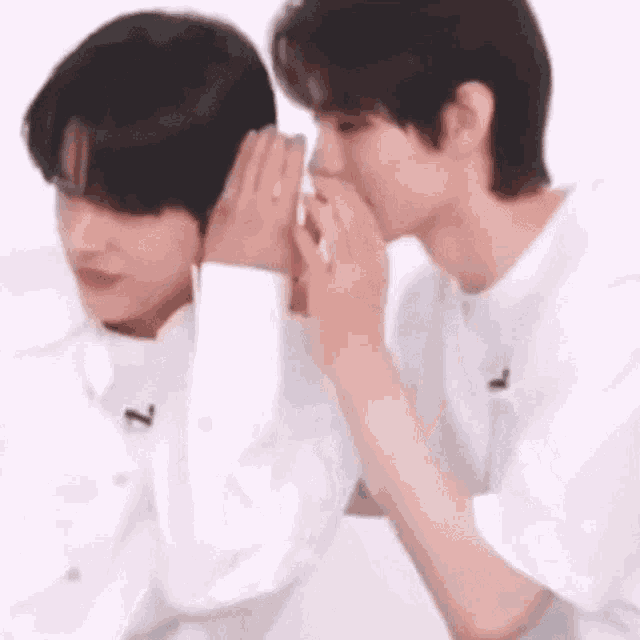 a man is whispering into another man 's ear while they are sitting next to each other .