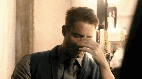 a man in a suit and tie is covering his face with his hands .