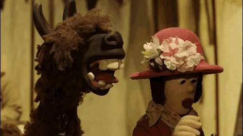 a woman in a red hat is standing next to a stuffed animal with its mouth open