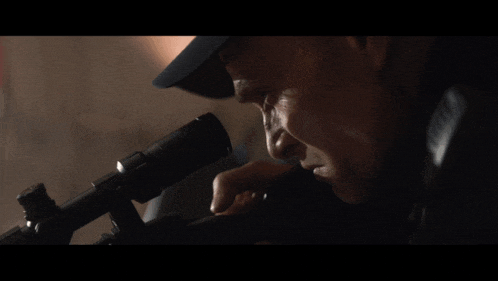 a man in a hat looks through a telescope at something