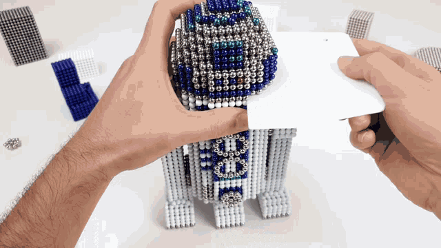 a person is holding a white card over a r2d2 toy made of magnets