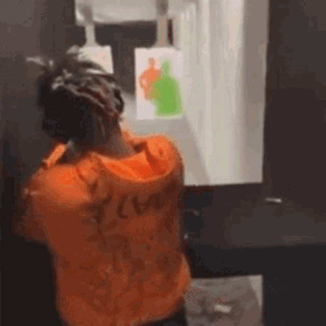 a man in an orange shirt is standing in front of a mirror .