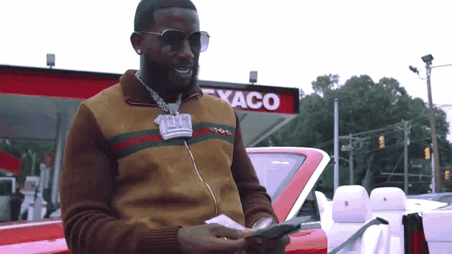 a man standing in front of a texaco gas station holding money