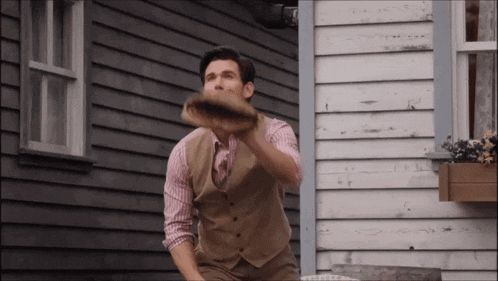 a man in a vest and plaid shirt is throwing a frisbee in front of a house