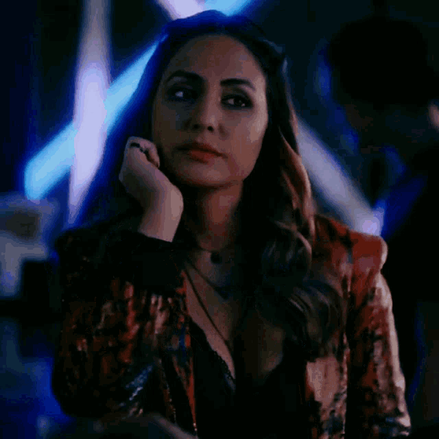 a woman in a plunging neckline top is standing in a dark room with blue lights behind her