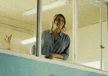 a woman is standing on a balcony looking out of a window and smiling .