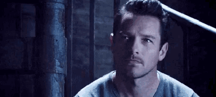a man with a mustache is standing next to a staircase in a dark room .