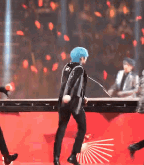 a man with blue hair is dancing on a stage in front of a microphone .
