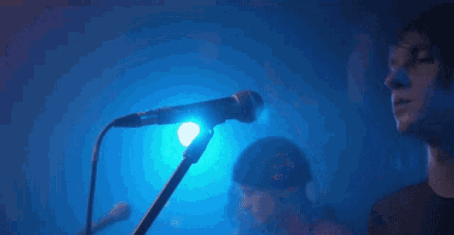 a man is singing into a microphone while another man plays a guitar in the background .