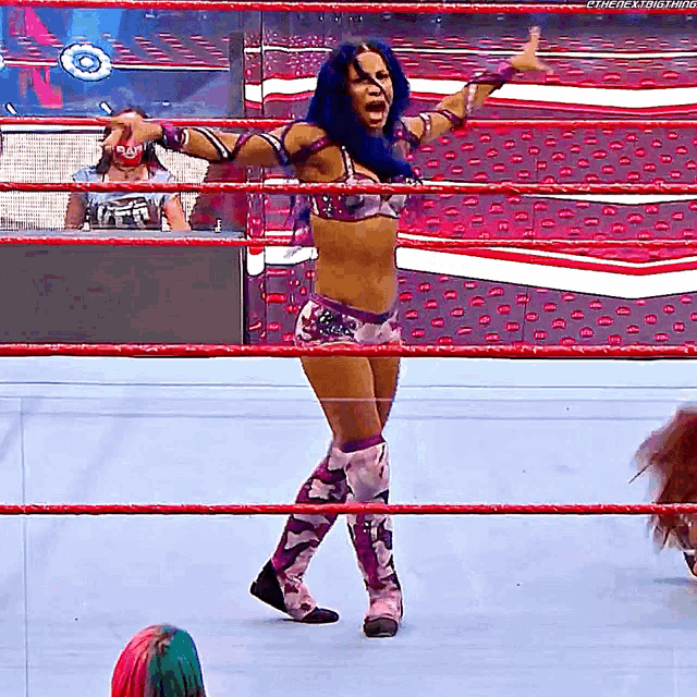 a woman with blue hair is standing in a wrestling ring with her arms outstretched .