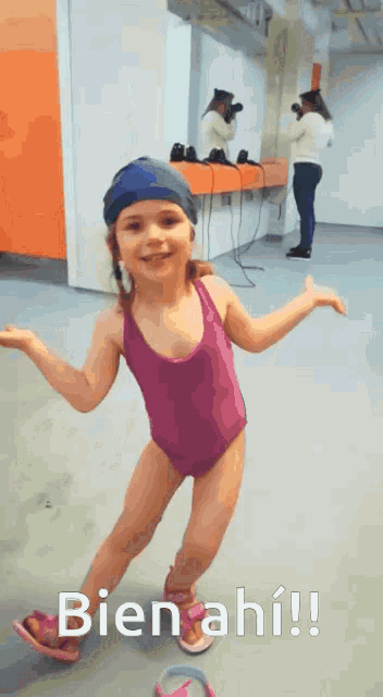a little girl in a pink swimsuit is standing in front of a sign that says bienahi