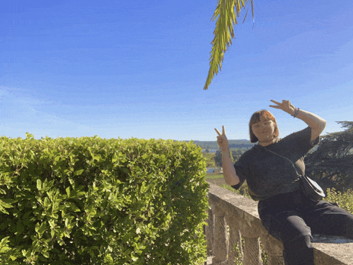 a woman giving the peace sign while sitting on a railing
