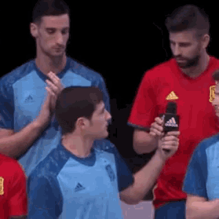a man in a red adidas shirt is holding a microphone in his hand