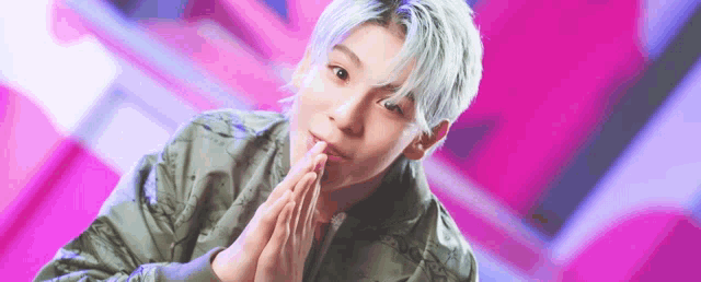 a young man with blue hair is wearing a green jacket and praying with his hands folded .