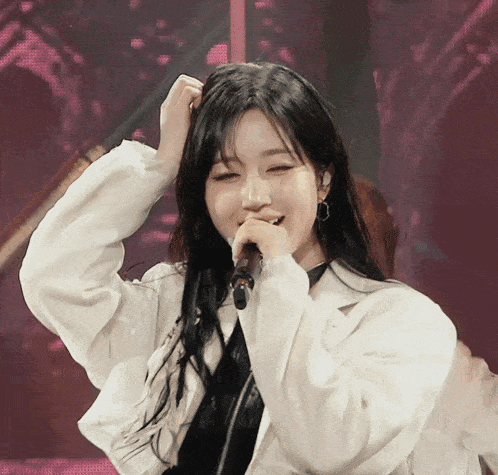 a woman in a white jacket singing into a microphone with her eyes closed