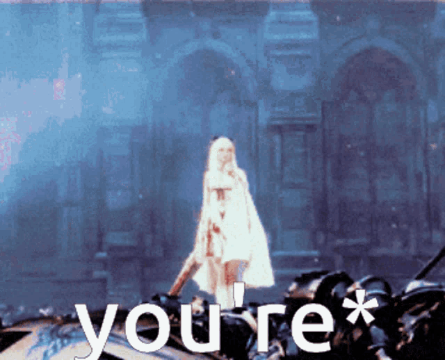 a woman in a white dress is standing in front of a building with the words " you 're * " written on it
