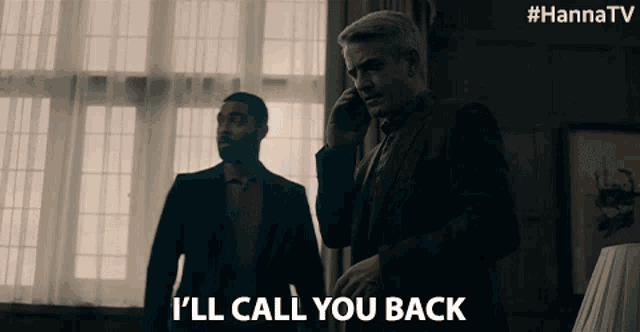 a man in a suit talking on a cell phone while another man stands behind him and says i ll call you back