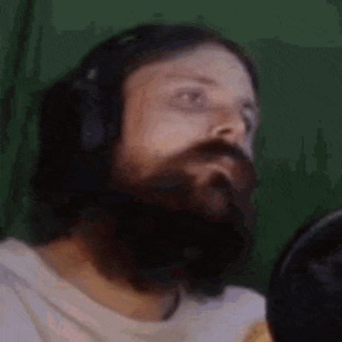 a man with a beard wearing headphones and a white shirt is looking at the camera .