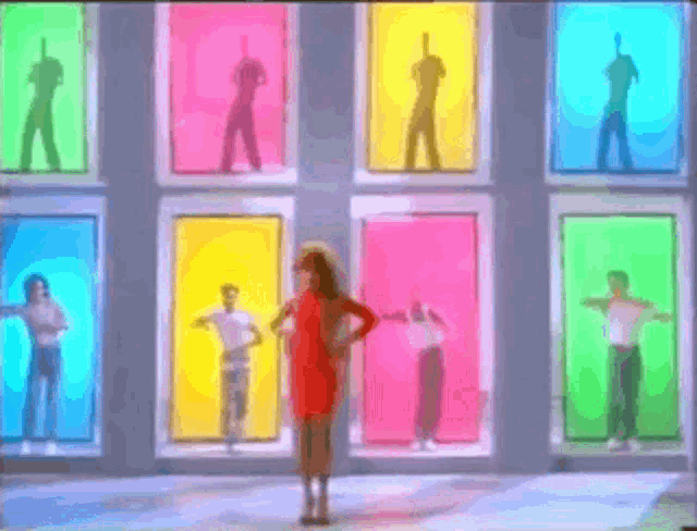 a woman in a red dress is standing in front of a group of people dancing in colorful boxes .