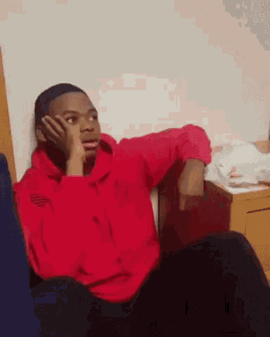 a man in a red hoodie is sitting in a chair with his hand on his chin .