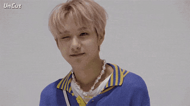 a man wearing a blue shirt and a pearl necklace