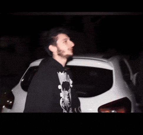 a man with a beard is standing in front of a white car .