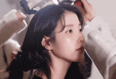 a close up of a woman 's face with a person applying makeup behind her