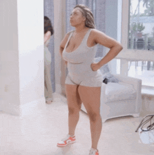 a woman in a tank top and shorts is standing in a room with her hands on her hips .