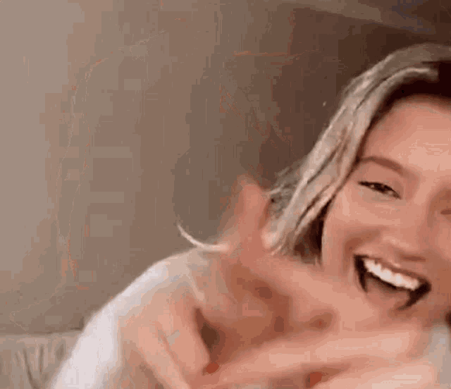 a woman is laughing and making a funny face while sitting on a bed .