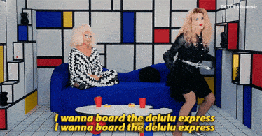 two drag queens are sitting on a blue couch and one of them is saying " i wanna board the delulu express "