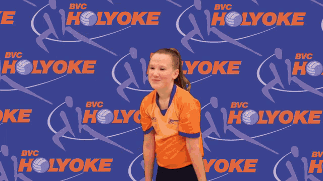 a girl in an orange shirt is holding a volleyball in front of a holyoke banner