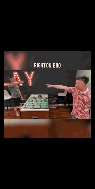 two men are playing foosball in front of a sign that says " right on bro "