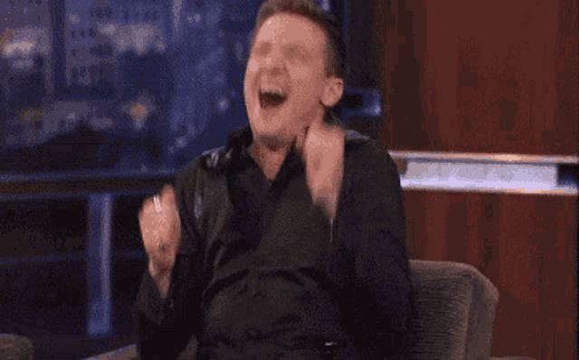 a man is sitting in a chair with his arms in the air and laughing .