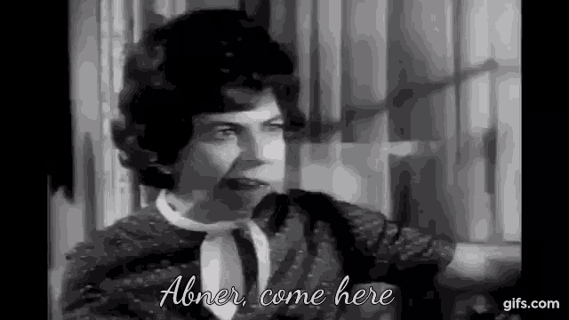 a black and white photo of a woman talking to another woman in a room .