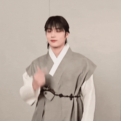 a young man is wearing a traditional korean dress and making a heart shape with his hands .